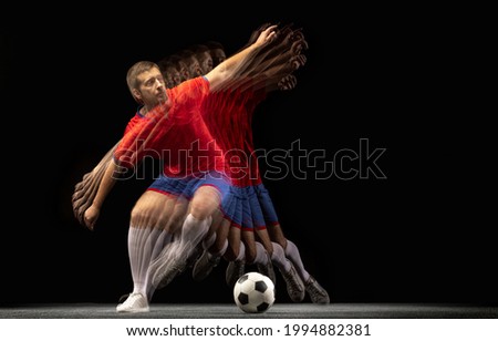 Non stop moving. Young caucasian football soccer player playing with ball in motion in mixed light on dark background. Concept of healthy lifestyle, professional sport, action, motion, hobby, team.