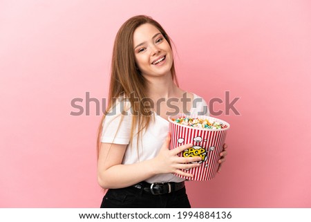 Teenager girl over isolated pink background holding a big bucket of popcorns