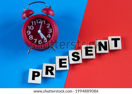 PRESENT - word on wooden cubes on a multi-colored background with an alarm clock. Info concept