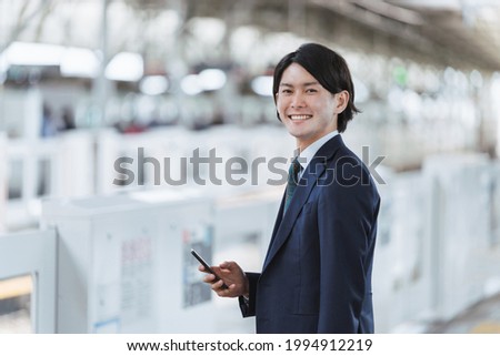 Image of young man commuting and IoT with a smartphone at the platform of the station