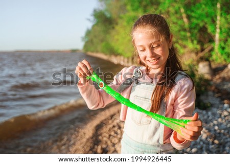 A little girl plays with slime on the riverbank