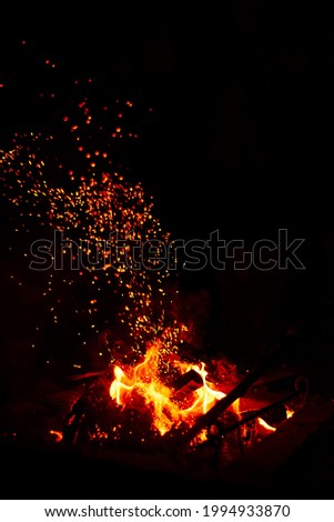 Burning red hot sparks fly from large fire in the night sky. Beautiful abstract background on the theme of fire, light and life. 
Fiery orange glowing flying away particles over black background.