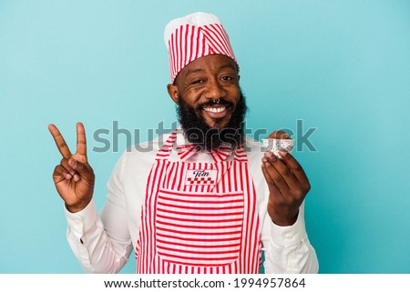 African american ice cream maker man holding an ice cream isolated on blue background joyful and carefree showing a peace symbol with fingers.