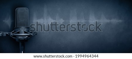 Studio microphone with audio waveform on concrete wall background. Podcast or broadcast banner with copy space. Royalty-Free Stock Photo #1994964344
