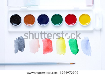 A set of watercolor paints, a paint brush and watercolor color blurs colors on a white background with a copy of the space. Close-up