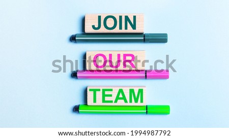 On a light blue background, there are three multi-colored felt-tip pens and wooden blocks with the JOIN OUR TEAM