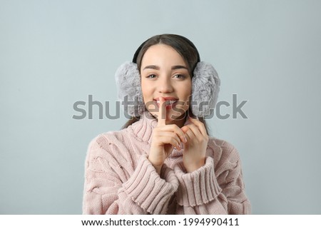 Beautiful young woman wearing earmuffs on light grey background