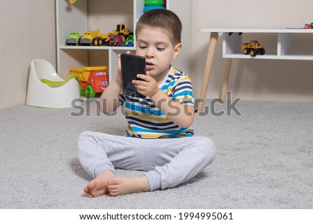 A little boy 3-4 years old looks into the screen of the tablet. Cartoons for children, screen time, children's dependence on the computer and phone
