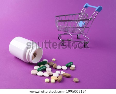 Mini shopping trolley and Bottle pills on purple background.