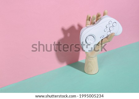 Wooden hand holding gamepad on blue pink pastel background. Trendy shadow. Concept art. Minimalism. Creative layout
