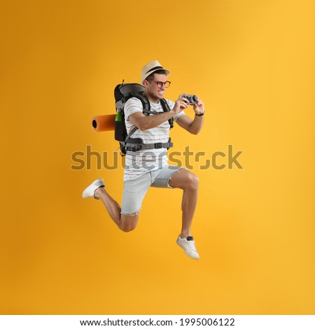 Male tourist with travel backpack taking picture on yellow background