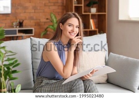 Beautiful woman with blank magazine in living room