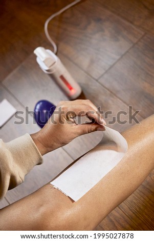 A close up image of a mixed race lady waxing her legs at home with a hair removal hot wax kit removing a wax strip