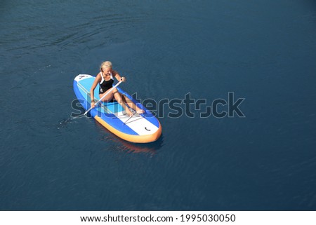 young girl in swimming suit riding  on sup surfing in the sea