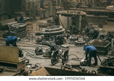 Large workshop with metallurgical plant workers working with cast iron parts, post-casting processing at steel mill foundry