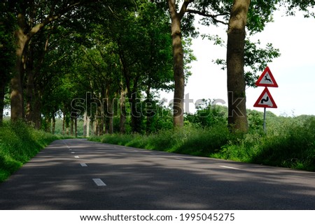 Road with traffic danger signs: warning for wild animals that may cross and junction on bend ahead