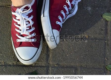 Photo of red classic sneakers with white laces on a background of concrete paving slabs

