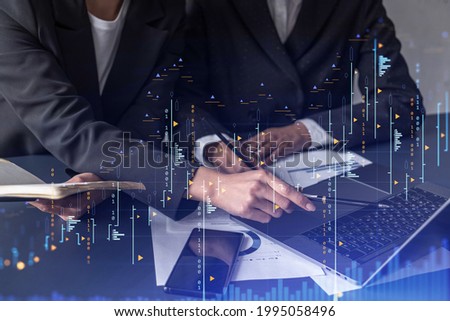 Two traders researching historic data to predict stock market behavior. Women in trading business concept. Forex and financial hologram chart over the table with the document. Royalty-Free Stock Photo #1995058496