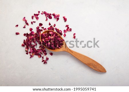 Dried rose petals in a wooden spoon, top view. Light background, copy space. Pink colored organic herb used for perfumes, cosmetics, teas and baths. Royalty-Free Stock Photo #1995059741