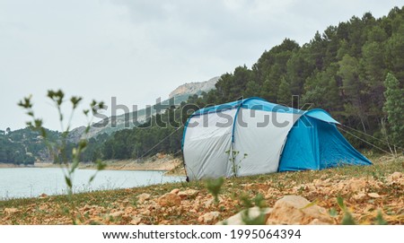 Tent on the shore of a lake with the forest and mountains in the background