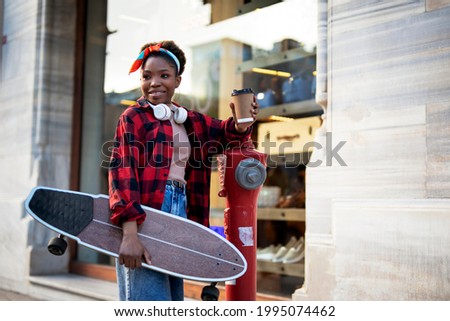 Portrait of happy african-american woman with skateboard. Young stylish woman with skateboard drinking coffee outdoors