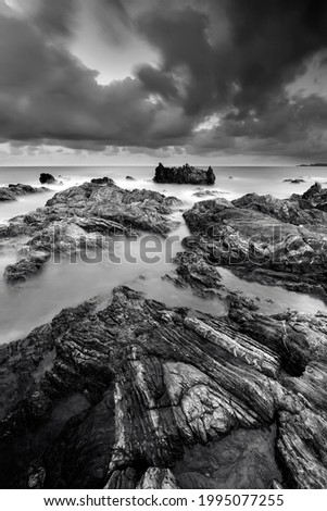 black white daytime long exposure rocky seascape scene A slow shutter speed was used to see the movement. soft and grain effect