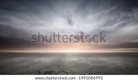 Dark Concrete Floor Background with Dramatic Sky Clouds and Sunset Horizon Royalty-Free Stock Photo #1995086993