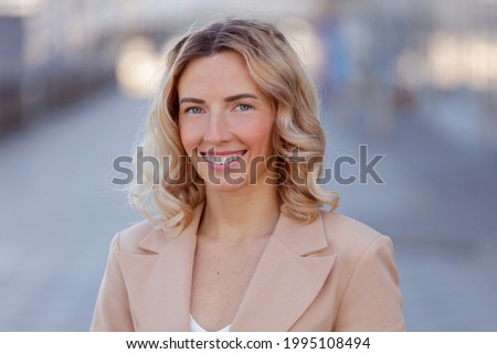 Headshot portrait of smiling young woman in suit outdoors. 