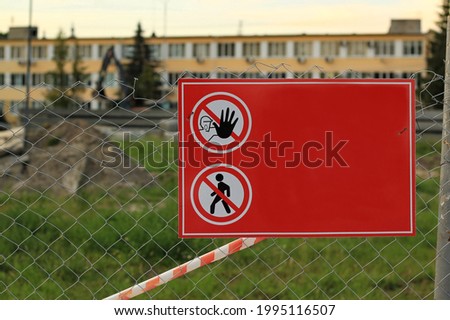 view of a metal mesh fence around a construction site with a red prohibition sign in summer russia