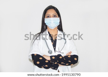 Female doctor wearing protective face mask with her arms crossed over white background