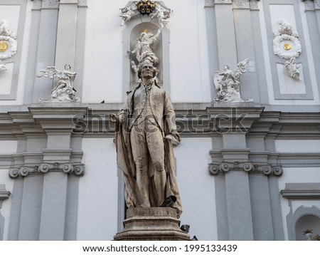 Gray statue in the city against the backdrop of ancient walls of the cathedral architecture. Authentic European sculpture of famous people. Classic old world urban outdoor photo.