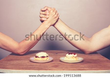 Two people are arm wrestling to decide on the best way of preparing a cream tea