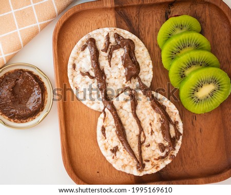 Rice crackers with peanut butter and chocolate-flavored cocoa, accompanied by kiwi slices