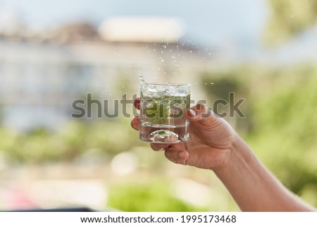 Man holds in his hands a glass of homemade cocktail of hard seltzer with herbs in front of mountains. Summer wallpaper close up. Royalty-Free Stock Photo #1995173468