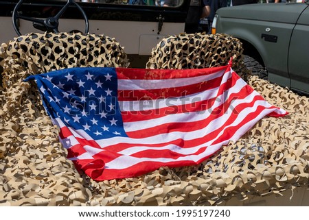 American flag stretched on a camouflage net on the back of a military car 