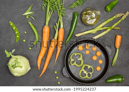 Sliced carrots and peppers in frying pan. Carrots with tops, asparagus and olive oil on table. Black background. Flat lay
