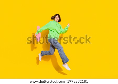 Full length body size view of pretty cheerful girl jumping carrying longboard isolated over bright yellow color background