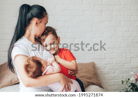 Young mother with two children and one kiss on the forehead.