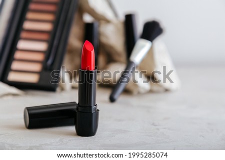 Red scarlet lipstick and set of decorative cosmetics for make up on gray concrete background with copy space. Minimalistic beauty aesthetic.