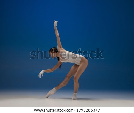 Art performance. Tender young beautiful ballerina, female ballet dancer dancing isolated on blue background. Beauty and grace. Concept of emotion, art, theater. Contemporary ballet. Copy space for ad.