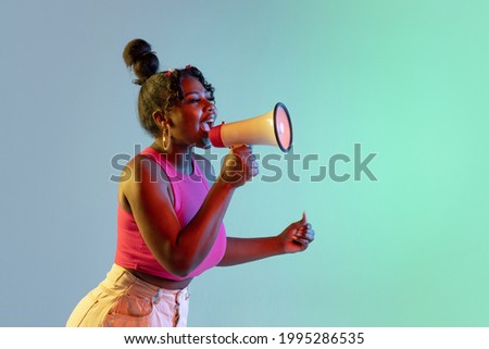 Profile picture of young beautiful African girl, female model speaking into megaphone isolated on blue green background in neon light. Concept of human emotion, facial expression. Copy space for ad.