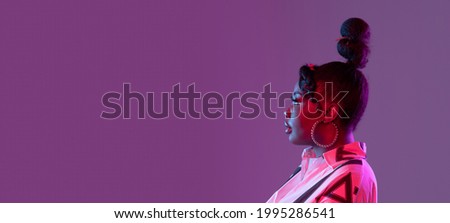 Flyer. Profile picture of young beautiful African girl, female fashion model isolated on purple background in neon light. Concept of human emotion, facial expression. Copy space for ad.