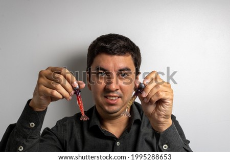 Brunette man holding two shrimps with different colors and jig head and hook attached. Mention the preparation for a day of family fishing on the beach, river or lake.