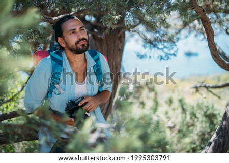Male photographer with a camera on a hike. Young handsome guy with a backpack and a professional camera takes pictures of nature on a hike among the trees in the mountains