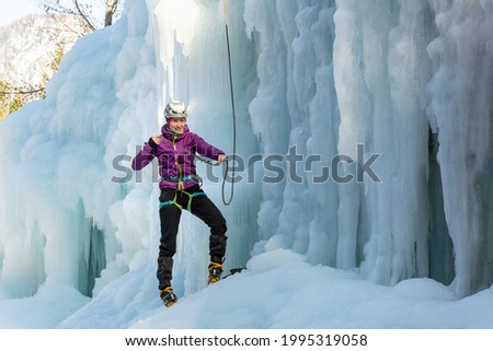 Woman ice climber tying a rope to his harness, preparing for a climb