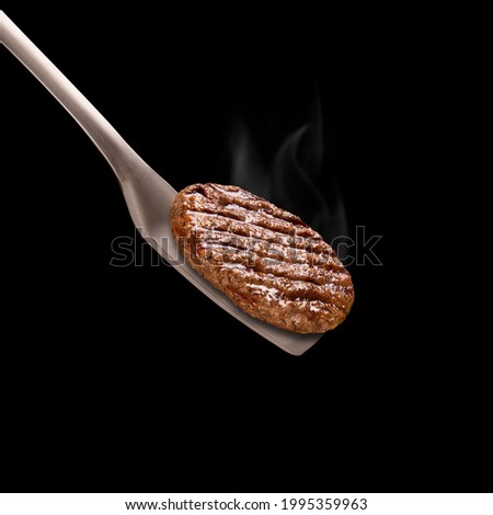 Grilled hamburger on a barbecue spatula isolated on black background