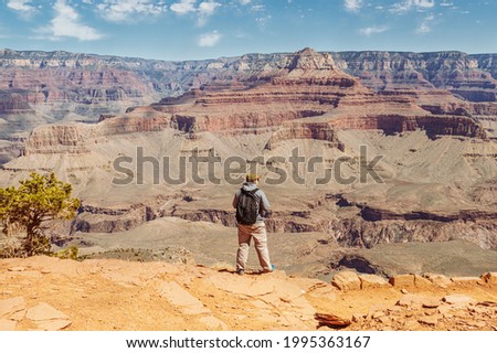 Vertical photo of a hiker-man standing on a cliff and looking at red formations of Grand Canyon