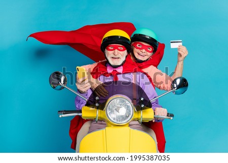 Portrait of two cheerful elderly retired pensioners riding moped using card buy order isolated over bright blue color background Royalty-Free Stock Photo #1995387035