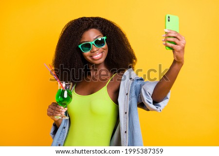 Photo of funny shiny dark skin woman wear jeans shirt drinking cocktail tacking selfie device isolated yellow color background