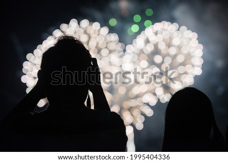Silhouettes of people taking pictures of heart shaped fireworks in the sky during an Independence Day holiday celebration in Boston, MA